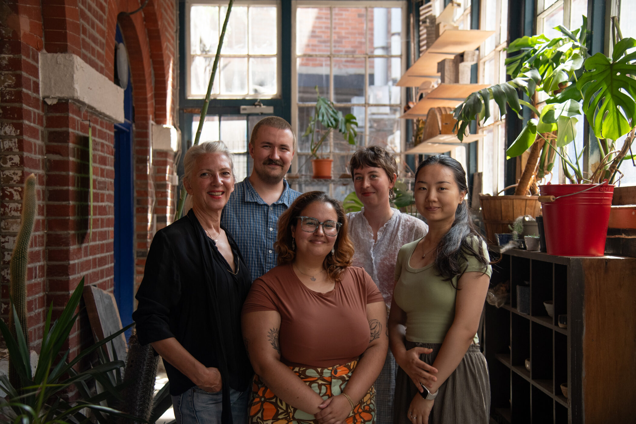 The five members of the Alternative Archiving Group standing together indoors, surrounded by plants.